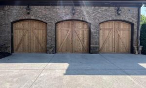 Three wooden garage doors on brick facade.