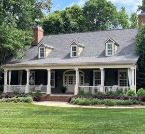 A gray house with a large porch and lawn.