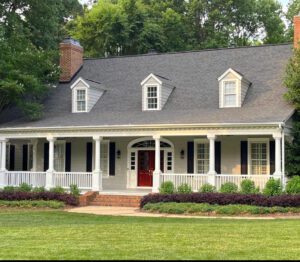 White porch house with red door and green grass.