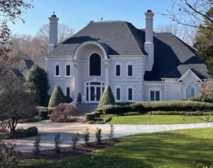 Large white house with black roof and driveway.