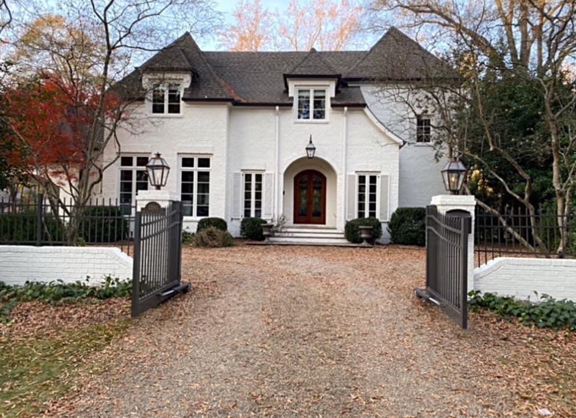 White house with gated driveway and fall leaves.