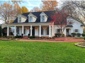 White house with porch and red leaves.